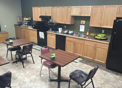 Hospitality service center room with tables, kitchen cabinets, coffee, and appliances.
